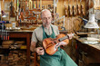 © Kzenon Premium - Instrument maker in his workshop checking finished violin