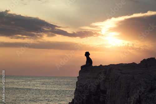Stampe mysterious boy sitting on the precipice of a cliff