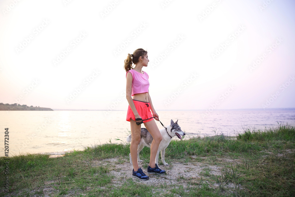 Young woman walking with husky on riverside