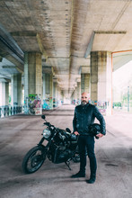 Mature Male Motorcyclist Standing By Motorcycle Under Flyover