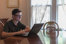 Teenage Boy Typing On Laptop In Dining Room