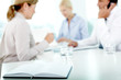 © pressmaster - Open record book on table against working business people
