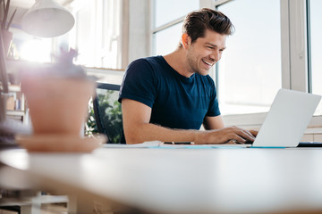 Wall Mural - Happy young businessman using laptop at his office desk