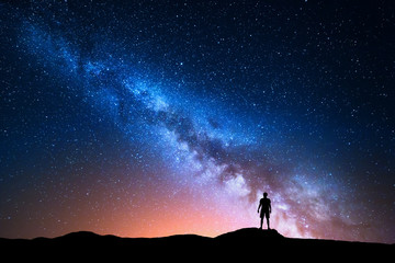 Wall Mural - Milky Way. Beautiful night sky with stars and silhouette of a standing alone man on the mountain. Milky way with red light and man on the hill. Background with galaxy and silhouette of a man. Universe