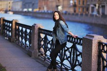 Beautiful Long-haired Girl Posing On The Waterfront In The Setting Sun  A Blurred Background River And St. Petersburg Architecture
