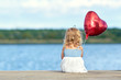 kleines Mädchen sitzt am Steg mit roten Ballon