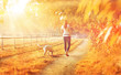 Gelbe Herbstlandschaft - eine junge Frau geht mit ihrem Hund spazieren während des Sonnenuntergangs