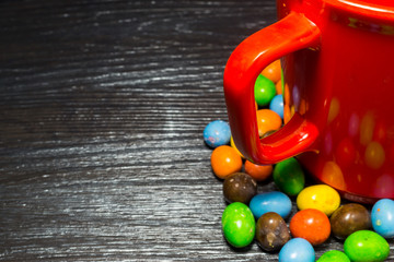 Colorful candy surround of red cup on black wooden texture backg