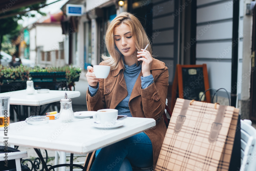 Beautiful blond woman sitting alone in cafeteria, smoking a cigarette and drinking  coffee. Stock Photo