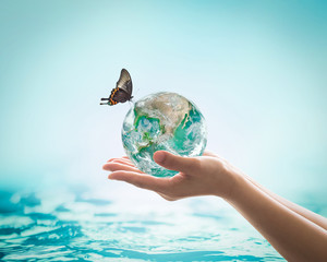 women's hands holding green planet w/ butterfly drinking potable water from globe on turquoise blue 