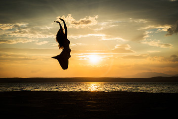 Successful woman jumping, dancing and having fun on sunset in beach. Freedom and happiness concept. Girl celebrating work out success.