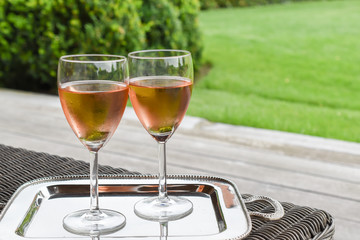 Two glasses of chilled rose wine presented on a silver tray with garden background.
Romantic celebration concept.