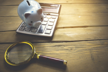 a magnifying glass on a wooden background and next to a piggy ba