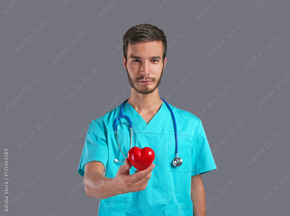 Handsome male doctor holding red heart on grey background