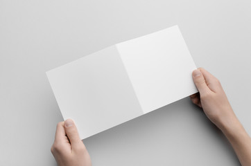 Wall Mural - Square Bi-Fold Brochure Mock-Up - Male hands holding a blank bi-fold on a gray background.