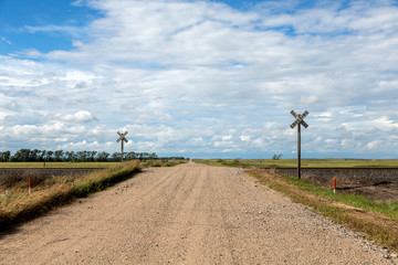 a gravel road and railroad crossing in north dakota on a summer day.