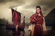 Viking woman with sword and shield standing near Drakkar on the seashore.