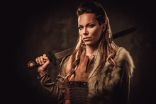 Viking Woman With Sword In A Traditional Warrior Clothes, Posing On A Dark Background.