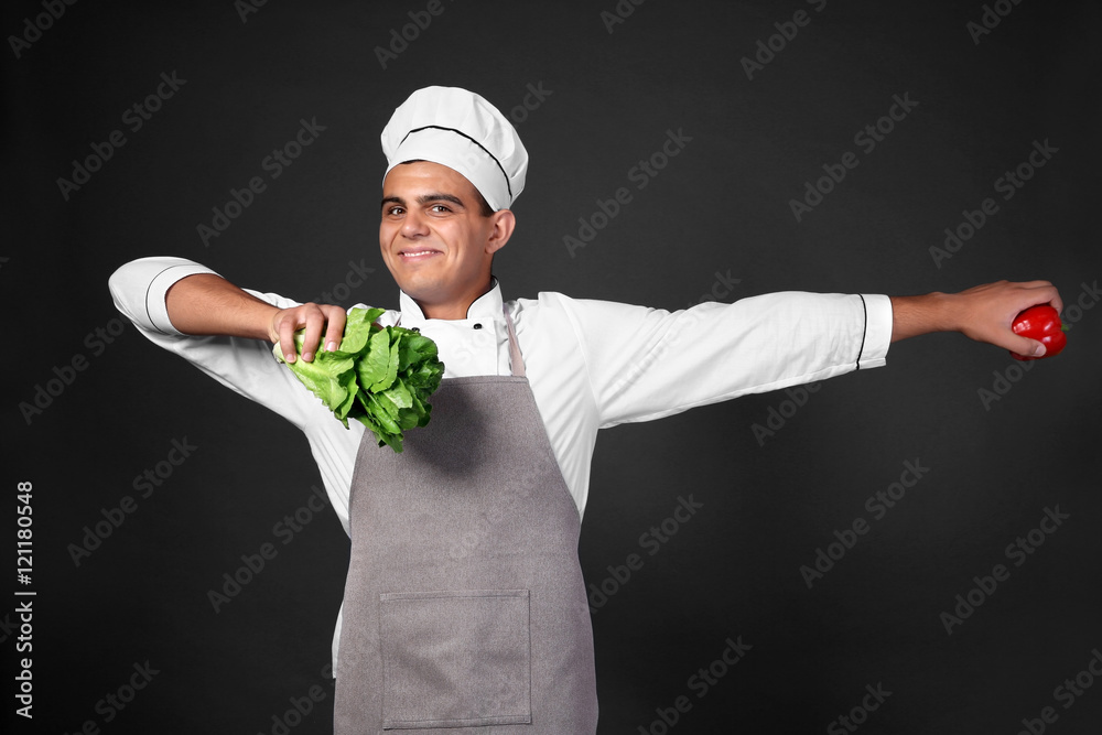 Young handsome chef cook with fresh vegetables on black background