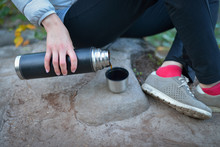 Young Woman, Sitting On Big Stone Preparing Hot Tea From Thermos Into Cap