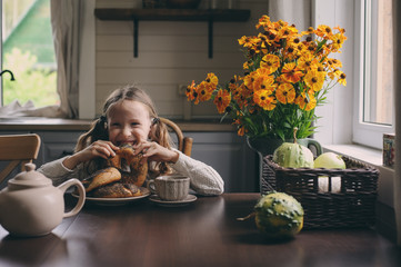 child girl having breakfast at home in autumn morning. Real life cozy modern interior in country house. Kid eating bagels and drinking tea.