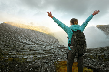 woman with backpacker enjoying view at top volcano ijen. indonesia.