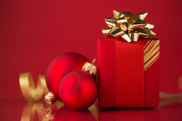 Wall Mural - red gift box with golden ribbons and xmas baubles on red background. merry christmas.