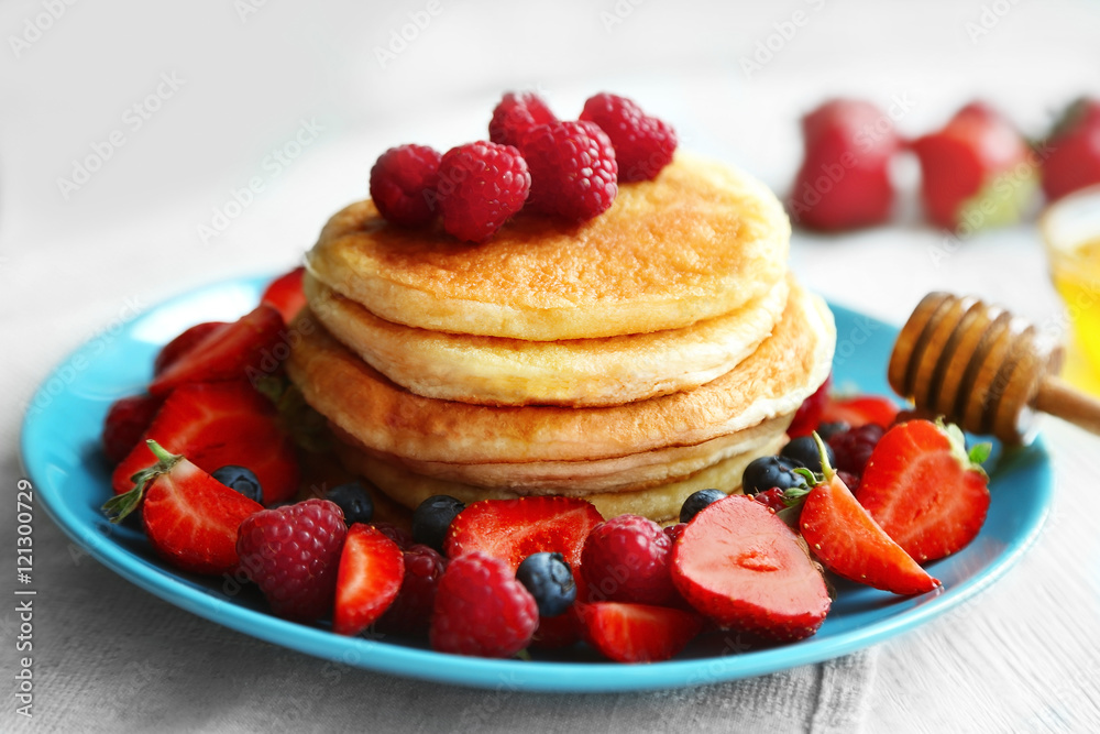 Tasty pancakes with fresh berries and honey on plate
