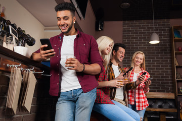 Wall Mural - People Friends Using Cell Smart Phone, Drinking Orange Juice Talking Laughing Sitting At Bar Counter, Mix Race Man And Woman