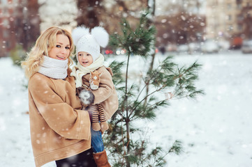 happy mother and baby daughter walking in snowy winter park. christmas family time.