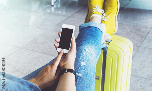 Plakat Młoda dziewczyna hipster siedzi na lotnisku w żółty zyski na walizkach podróży w Europie, kobiece ręce wiadomości SMS na gadżet w hali terminali, podróżnik podróż podróży koncepcja, pusty mockup
