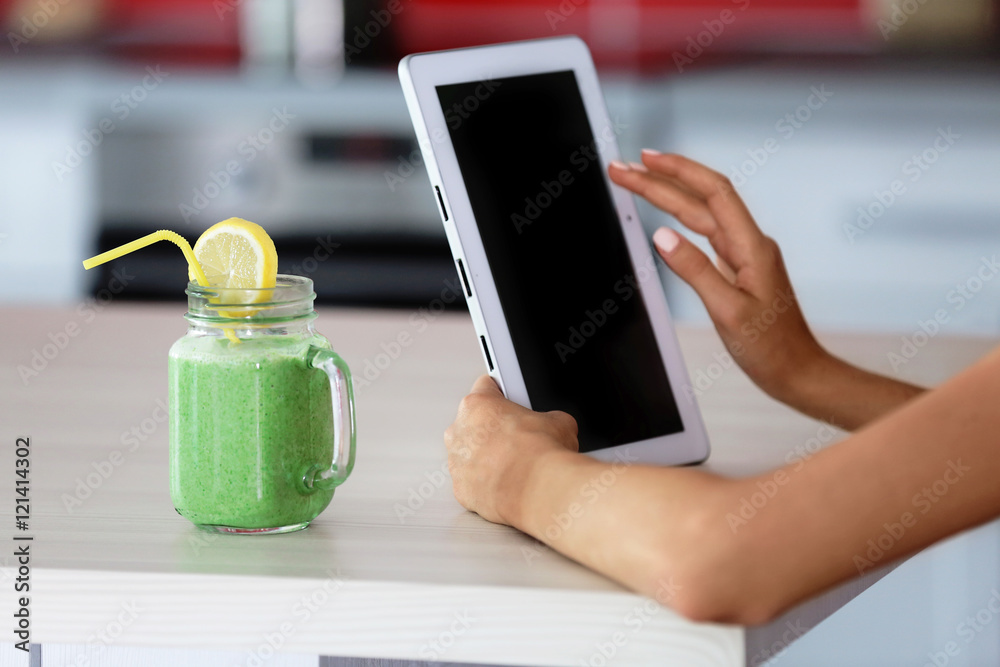 Girl with tablet and smoothie calculating calories on kitchen