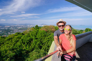 Wall Mural - Tourist attraction. Couple of travelers taking selfie enjoying sea, city and sky on the view point.