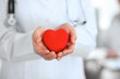 © rogerphoto - Female doctor with stethoscope holding heart.  Patients couple sitting in the background