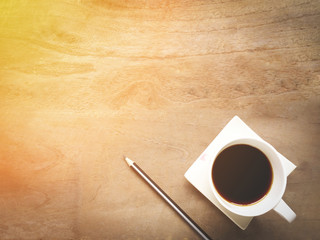 Coffee cup and pencil on wood table in the morning light, top view with copy space.