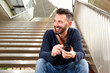 © mimagephotos - Happy mature guy with cellphone sitting on steps