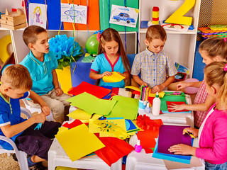 Wall Mural - Group of school children are making something out of colored paper on table in primary school. Children craft lesson in primary school. Development children craft at class in school.