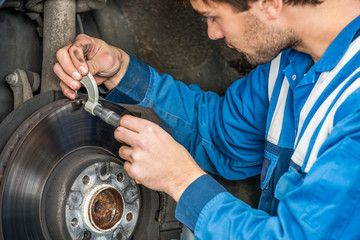 Male Car Mechanic Examining Brake Disc With Caliper