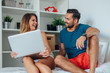 © jakubzak - Young woman and man are sitting on the bed and using laptop pc w