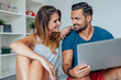 © jakubzak - Young couple is sitting on the bed and using laptop pc to online