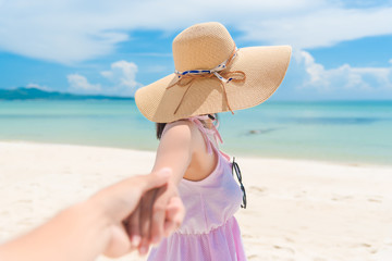 Woman walking on romantic honeymoon beach holidays holding hand of boyfriend following her, view from behind. A young girl holding hands on the beach.