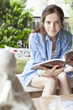 © PhotoAlto - Portrait of young woman reading book while sitting outdoors