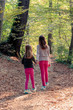 Older and younger sister holding hands and walking in city park forest in autumn