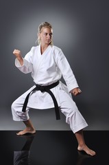 Beautiful young black belt female karate doing kata on the gray background