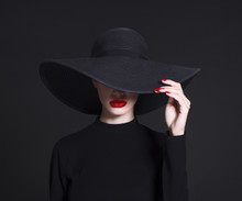 Luxury Woman In A Large Black Hat And Bright Lips On Black Background