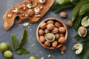 Wall Mural - Wooden bowl with fresh walnuts, leaves and nut shell on gray stone background. Autumn seasonal.