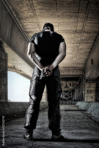 Cuadros en Lienzo Man in black uniform and mask standing with gun