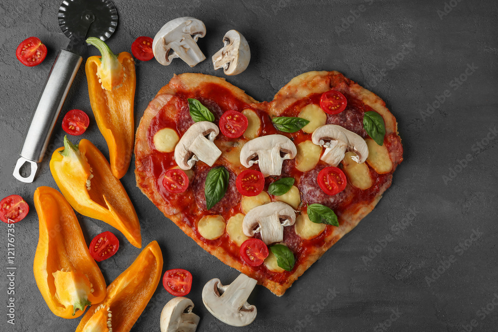 Tasty pizza in heart shape with pepper and tomato slices on table