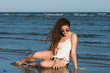 © Domforstock - Woman with long curly hair wear bottom bikini, sunglasses and white shirt, sitting in sea water. Sea and sky as background