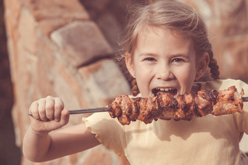 Little beautiful smiling girl with pleasure eats kebab outdoor a